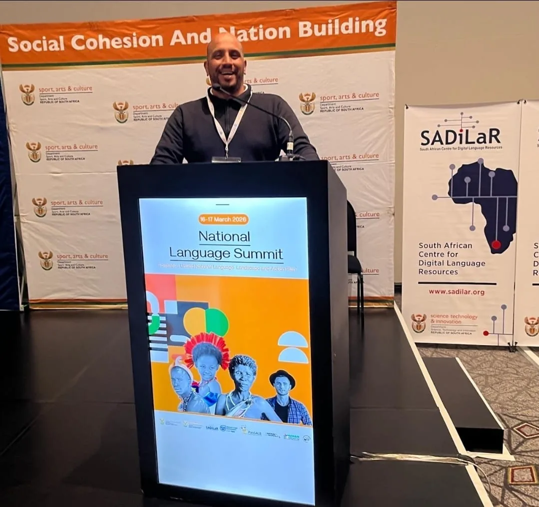 Speaker addressing the National Language Summit from the podium beneath the Social Cohesion and Nation Building banner