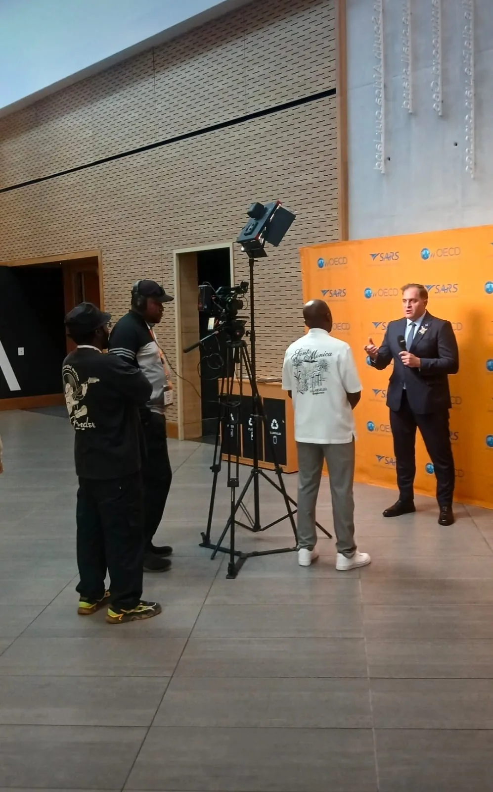 Broadcast crew filming an interview against the SARS and OECD branded backdrop